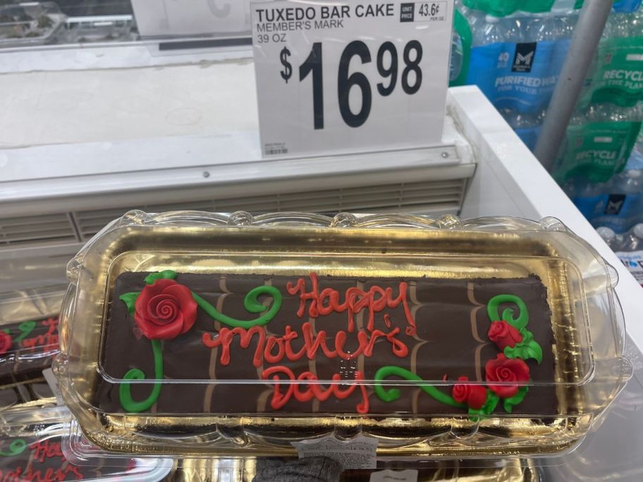 a womans hand holding a chocolate bar cake decorated with happy mothers day written across it in red icing