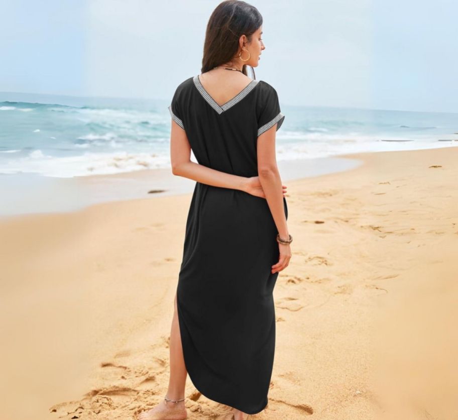 a woman wearing a black short sleeve maxi dres standing on a sandy beach