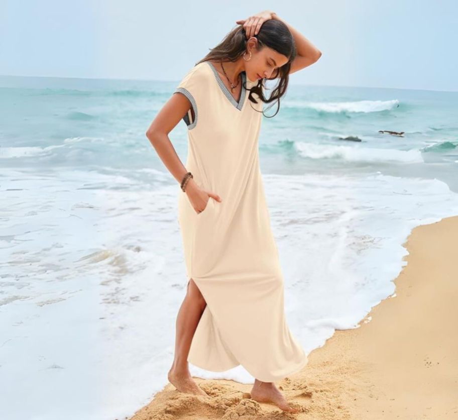 a woman wearing a khaki short sleeve maxi dress standing on a sandy beach