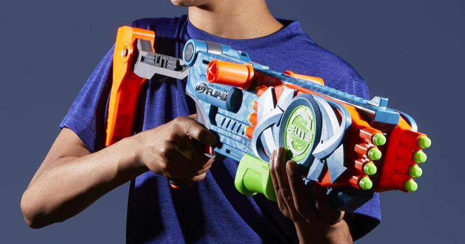 boy holding a large blue, orange, and green nerf blaster