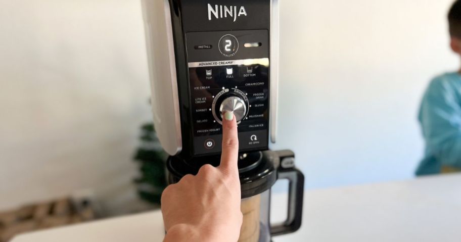 Hand pushing the button on a Ninja Creami Deluxe