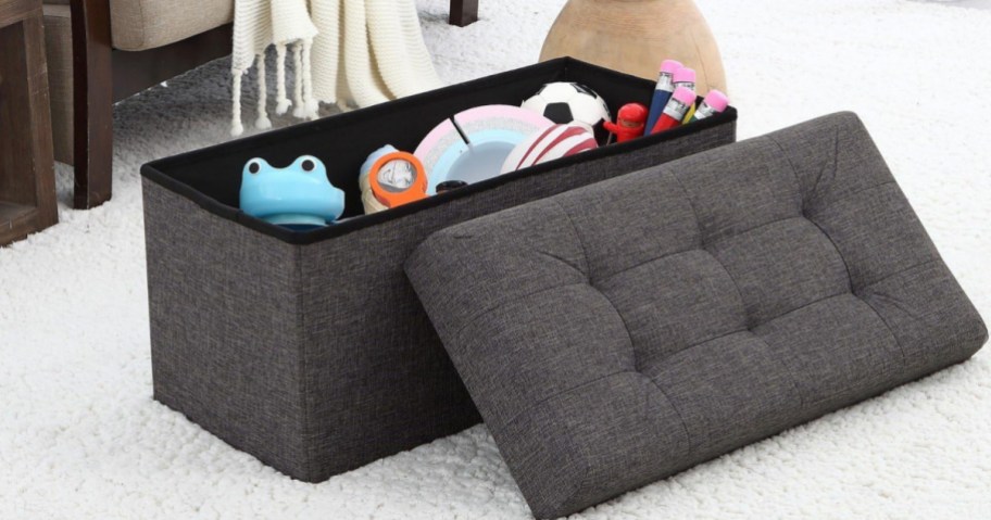 Dark gray ottoman filled with toys next to bed