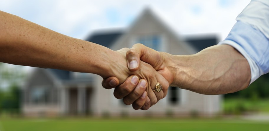 Two people giving a handshake in front of a home