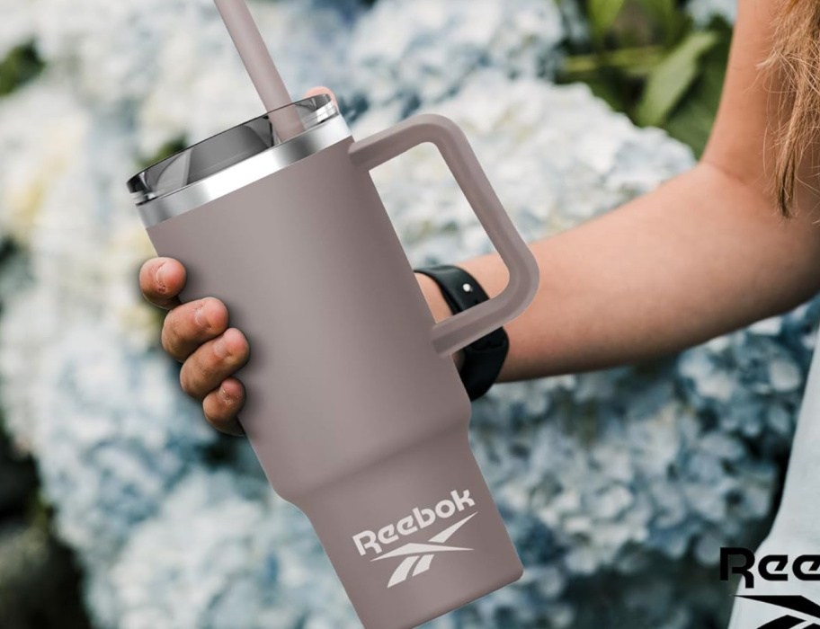 woman holding reebok gray tumbler in front of white flowers