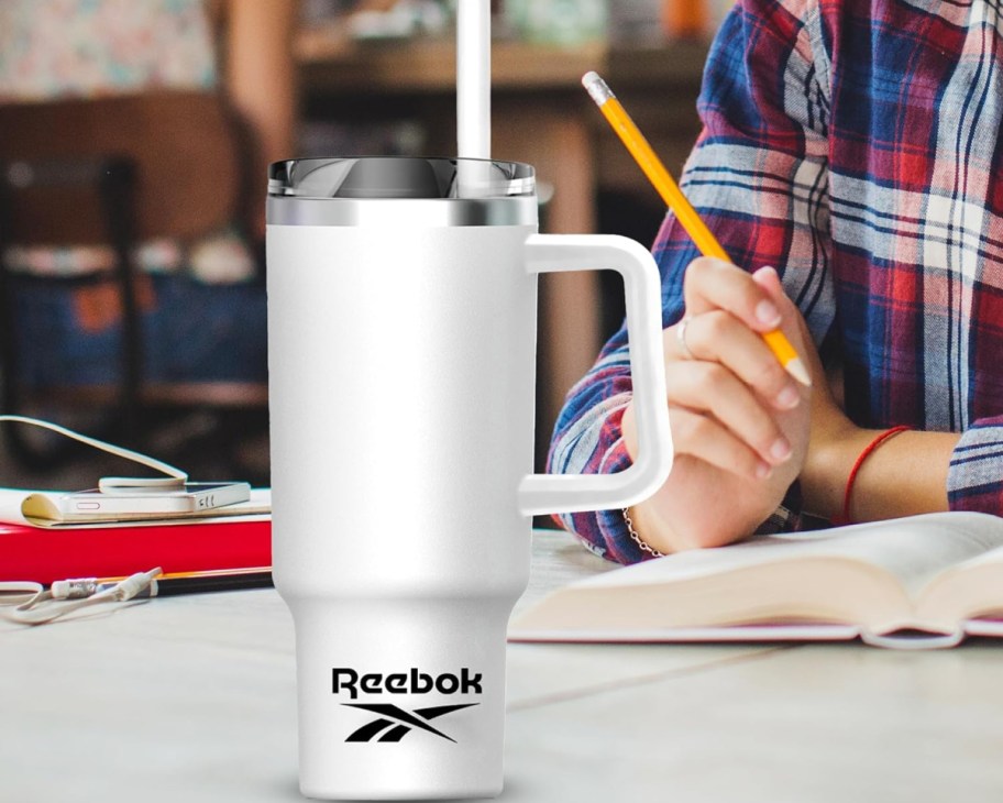 Reebok tumbler in white displayed on the table while someone writes in the background