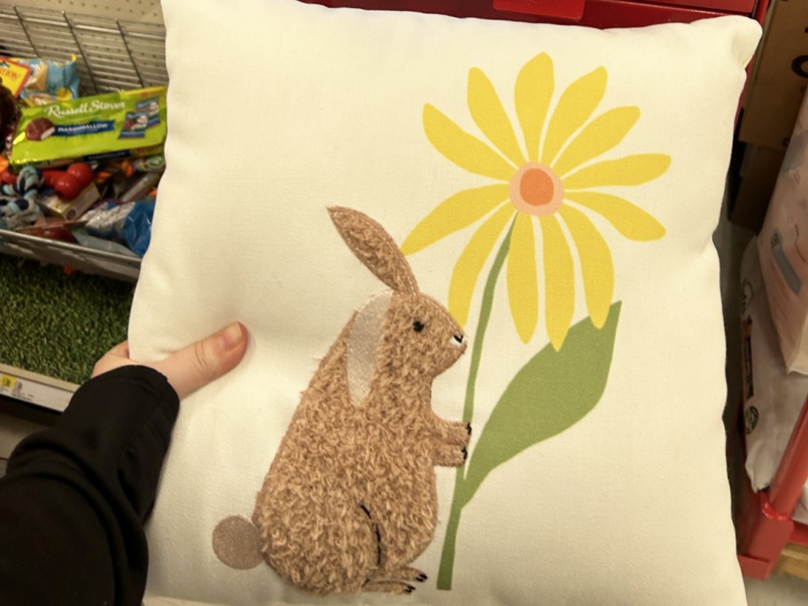 hand holding a throw pillow of a bunny holding a flower
