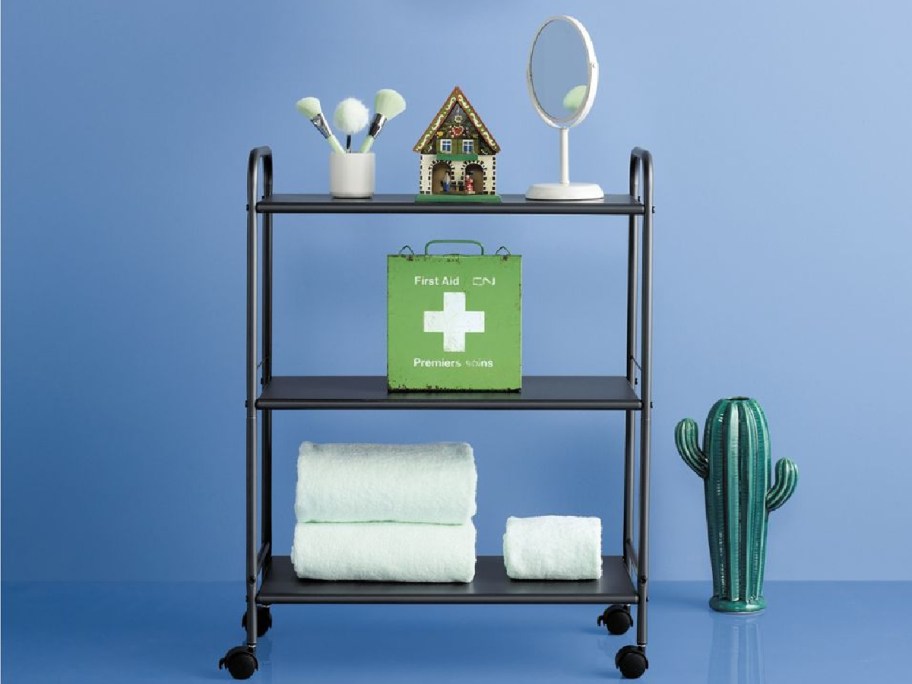 A room Essentials metal 3-tier utility cart with knick knacks and towels on it