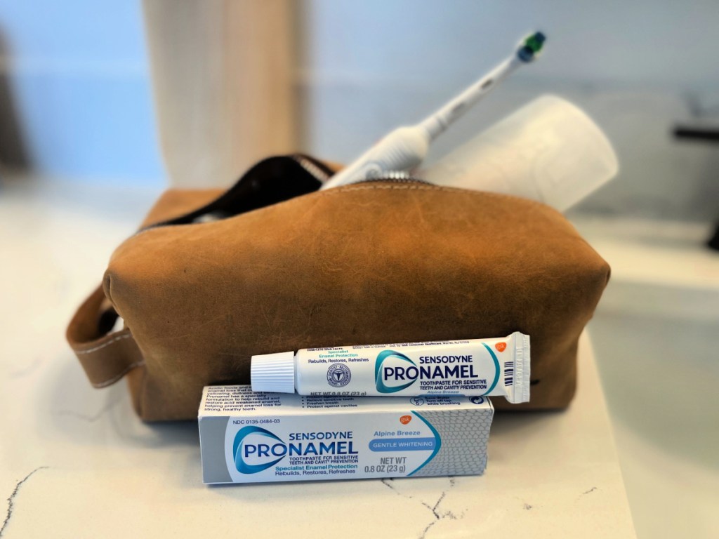 Travel size tube of Sensodyne ProNamel toothpaste on bathroom counter in front of travel bag