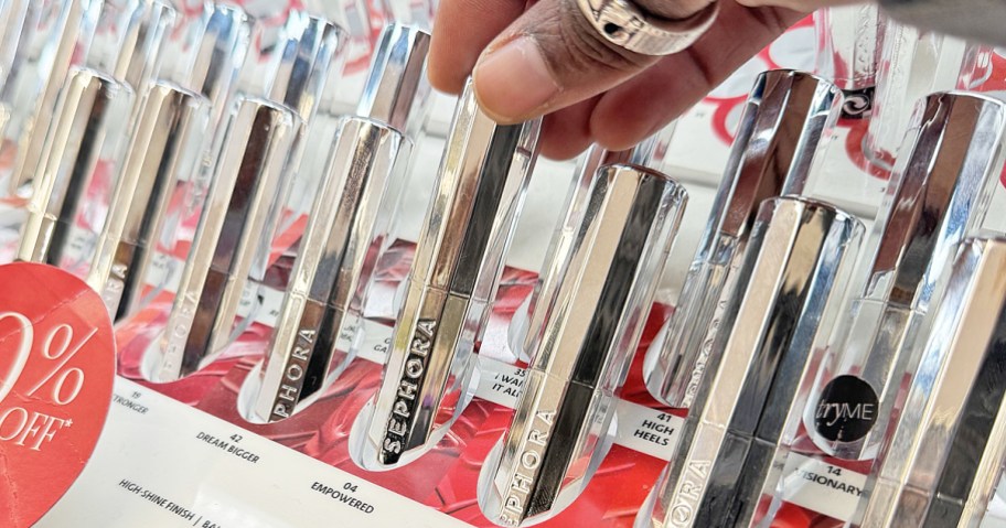 hand grabbing a silver tube of lipstick from store display