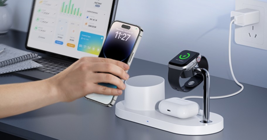 hand placing an iphone on a charging station that has airpods and an apple watch on it