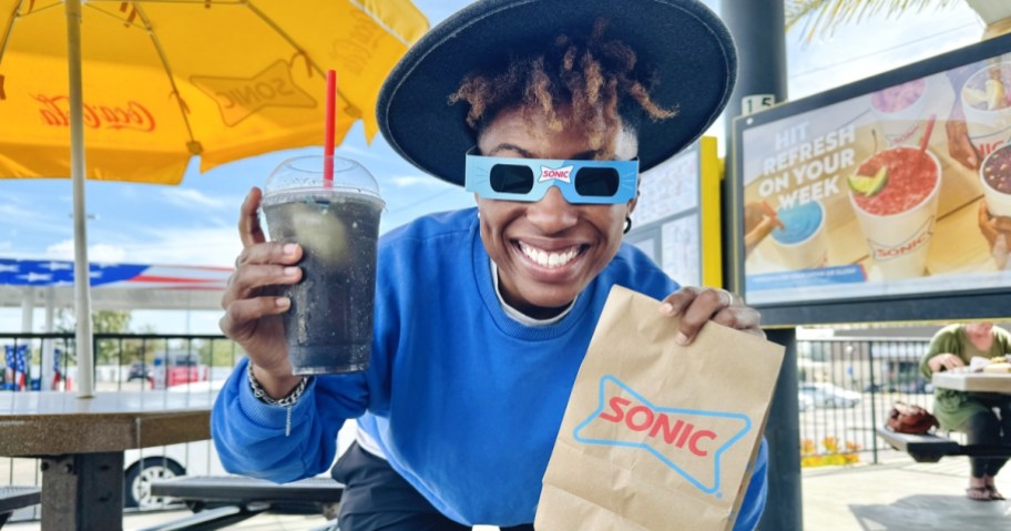 woman wearing sonic eclipse glasses holding bag and blackout slush