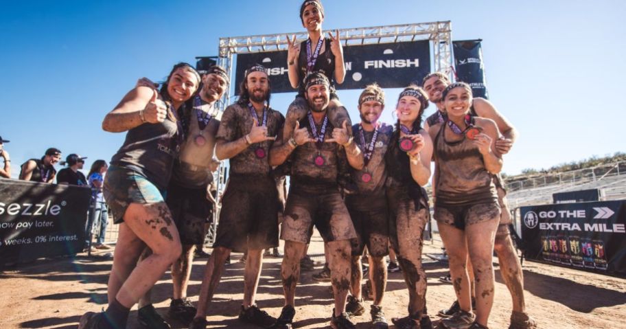 A group of men and women wearing medals posing at the finish line of a Spartan Race