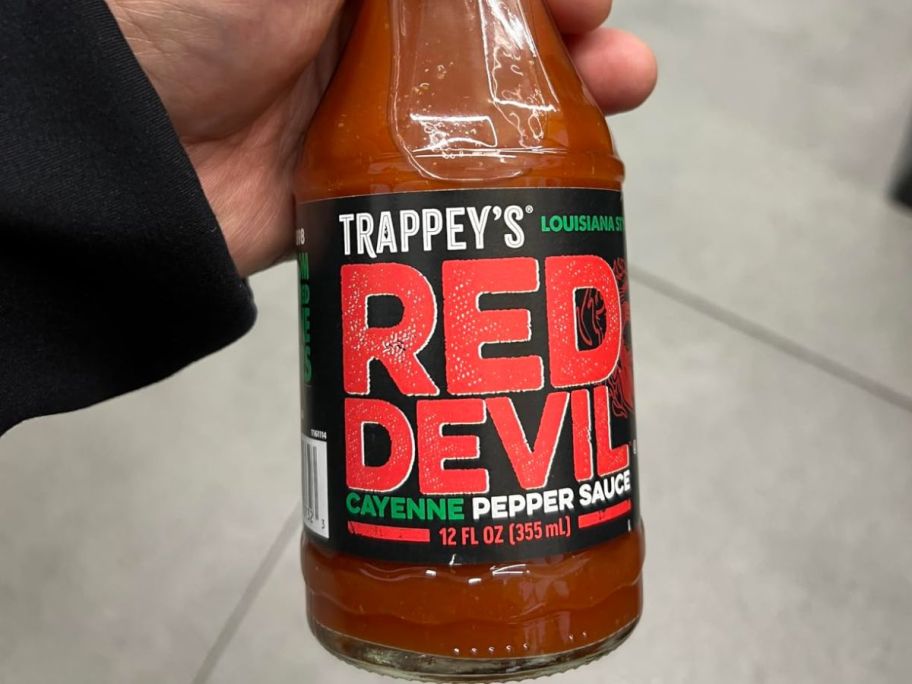A hand holding a bottle onf Trappey's Red Devil Cayenne Pepper Sauce