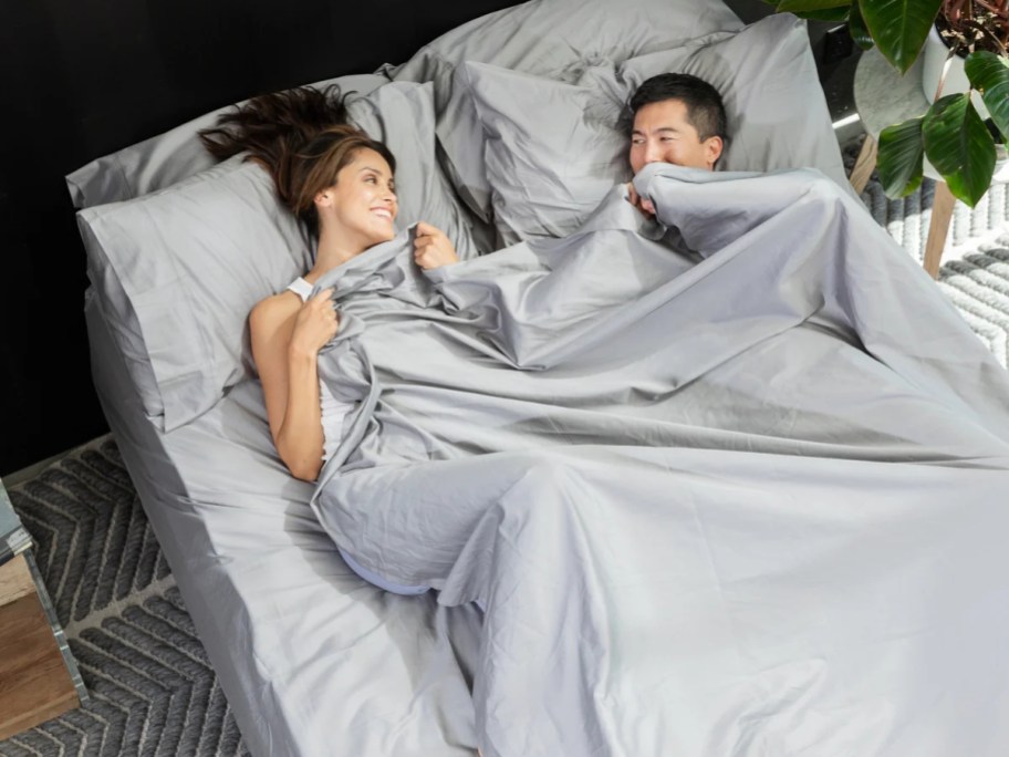 man and woman laying in a bed with grey sheets