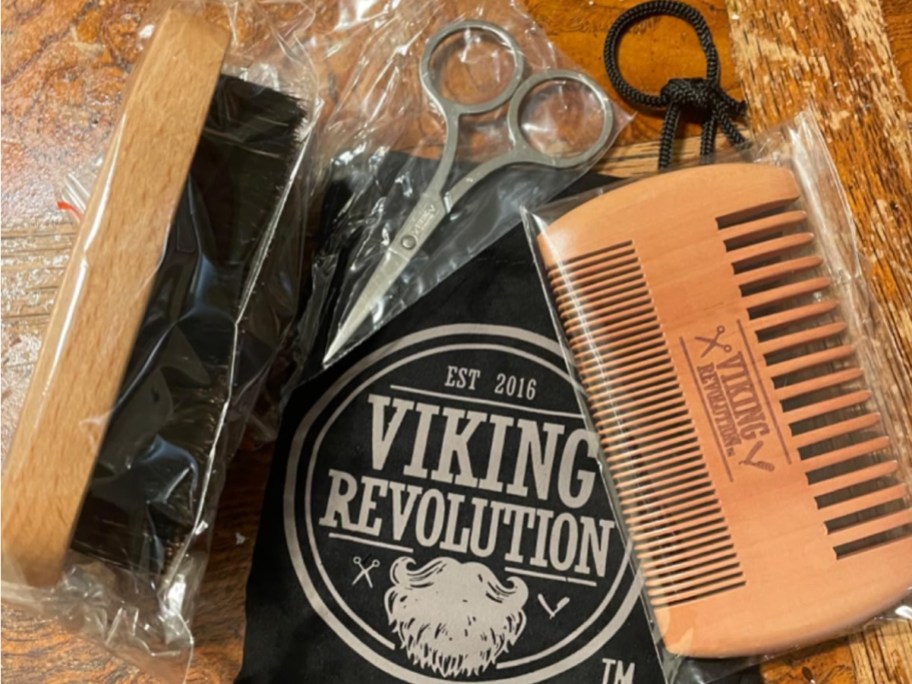 A Viking Revolution beard brush, scissors, and comb laying on a storage bag with the Viking Revolution logo on it