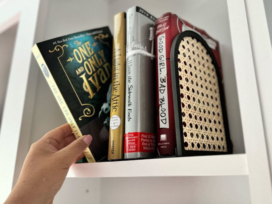 Bookshelf with a hand reaching for a book between metal and rattan bookends from Walmart