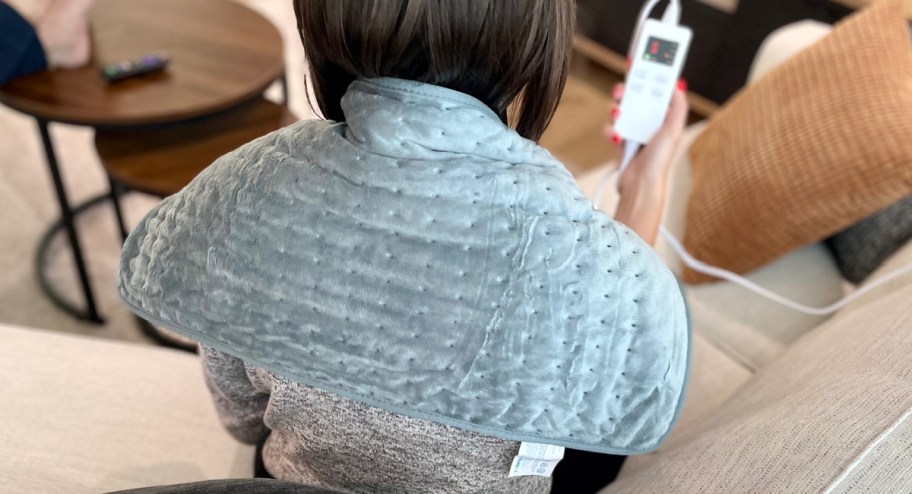 Woman using large heating pad on her back while holding remote control