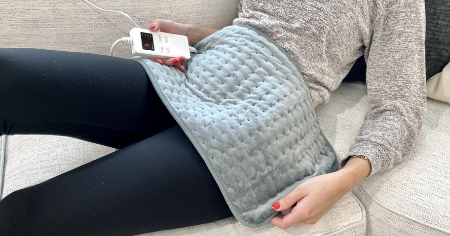 woman sitting on couch with grey heating pad on her lap