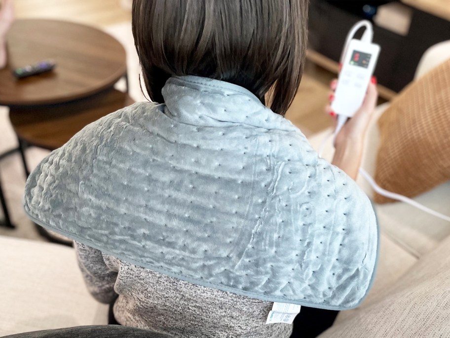 woman sitting with grey heating pad on her shoulders