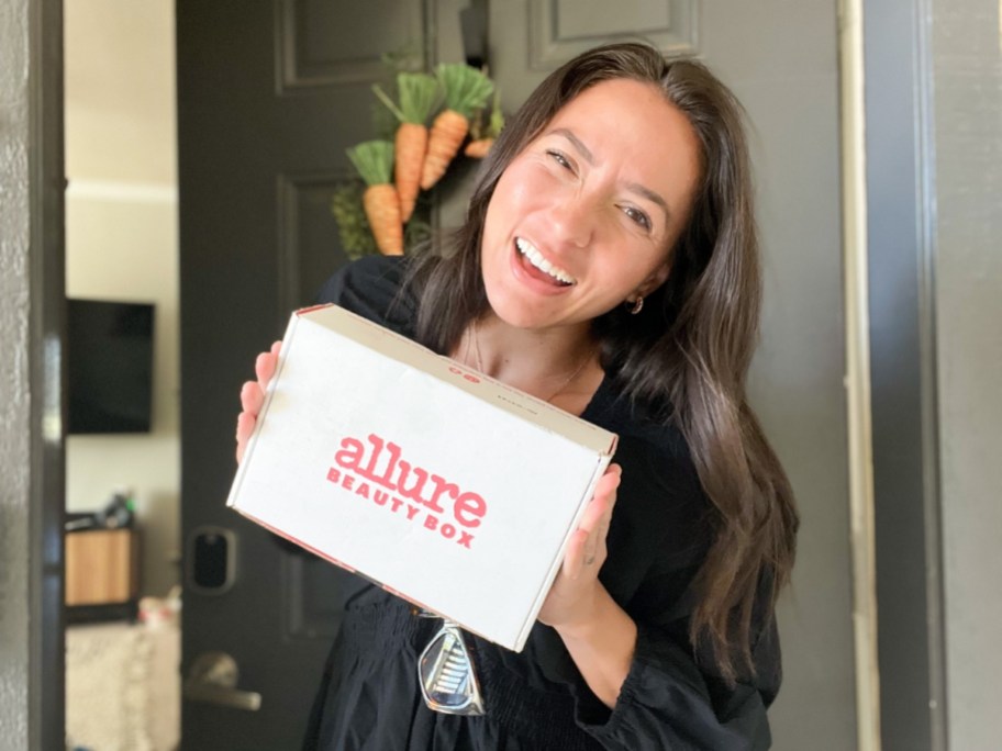 woman standing outside her front door holding an Allure Beauty Box