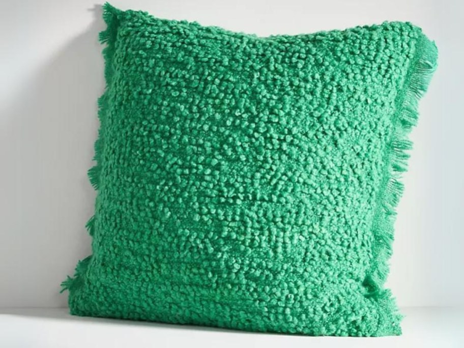 green boucle style pillow leaning against a wall