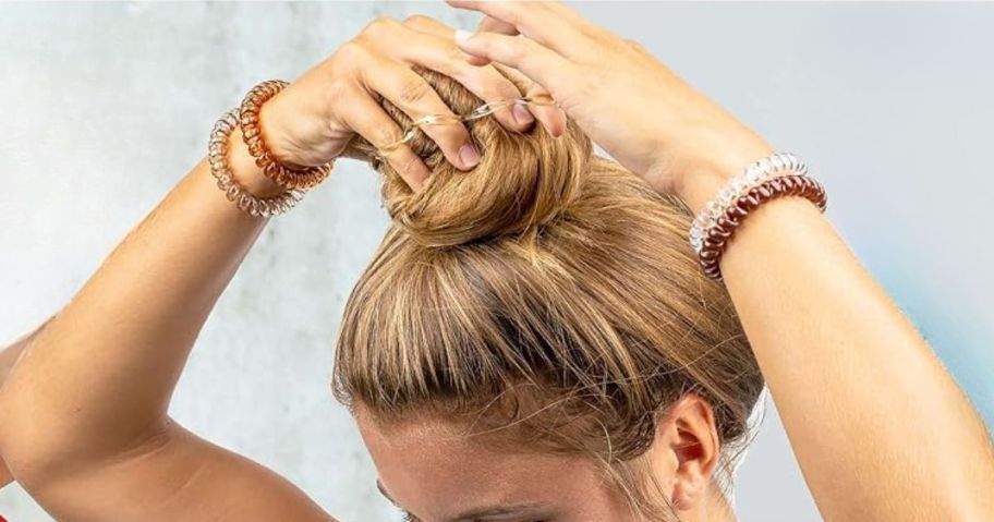 woman putting her hair in a bun with a spiral coil hair tie with more spiral coil hair ties on her wrists