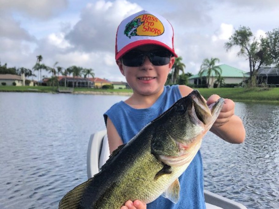 little boy in a bass pro shops hat holding a large fish