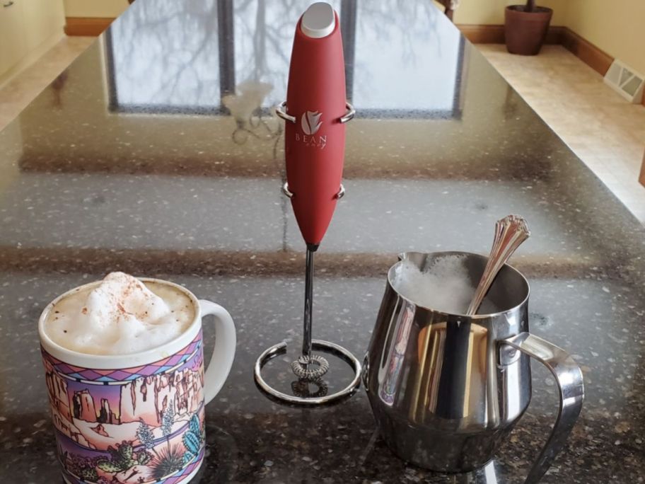 bean envy milk frother in red sitting on counter next to coffee