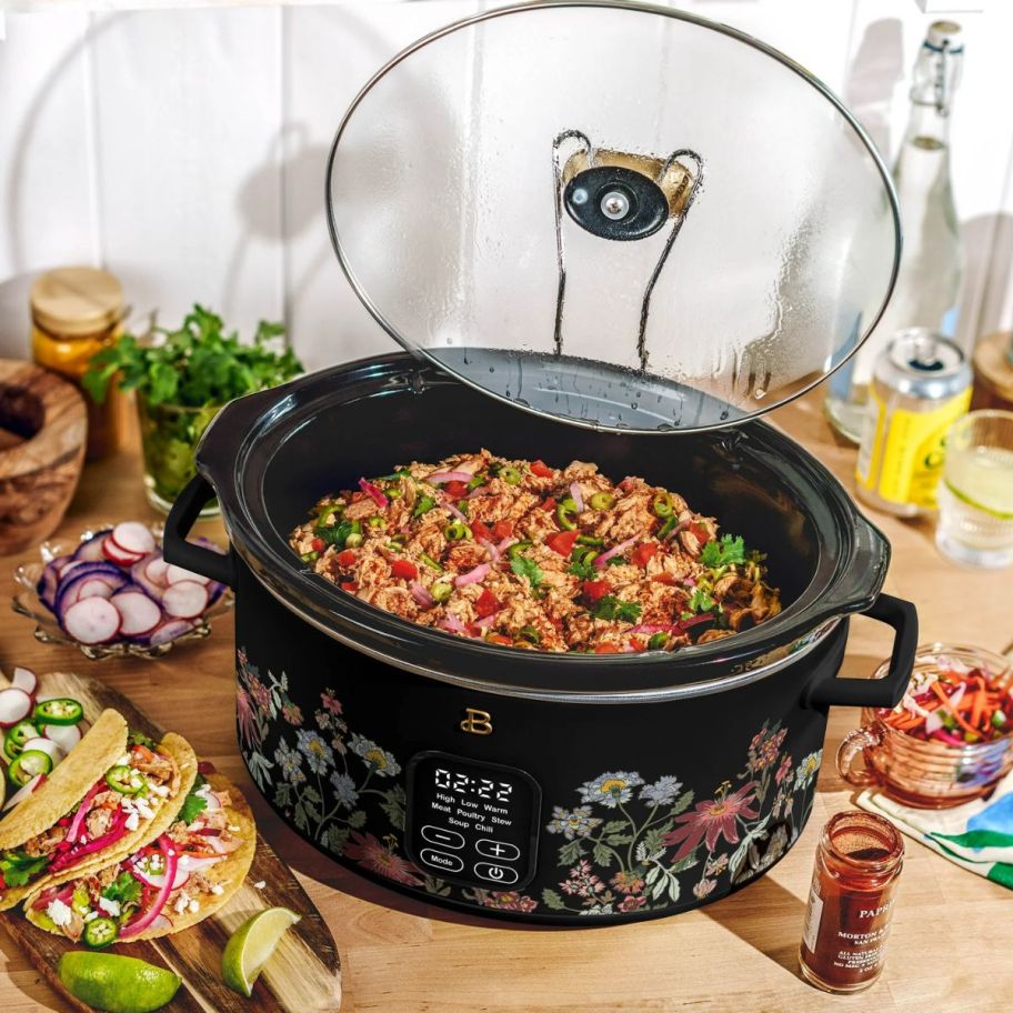 A slow cooker is shown with food, with the lid open and resting on a kitchen counter.