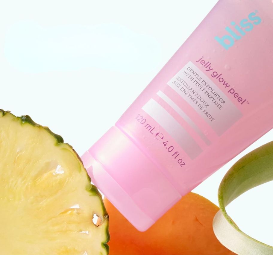 a tube of skin exfoliant shown with a pineapple slice and a fresh orange