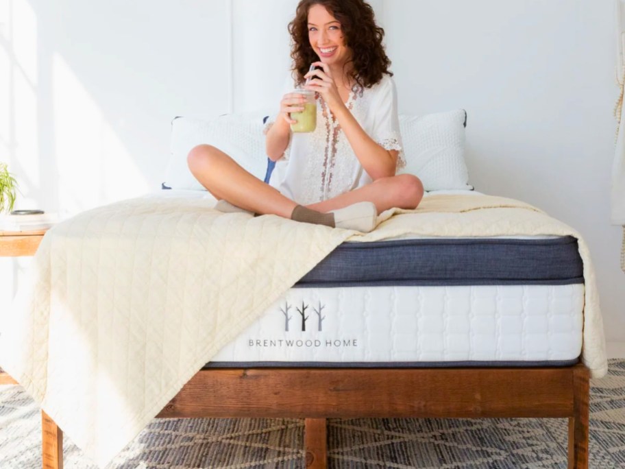 woman drinking a smoothie while sitting on a bed