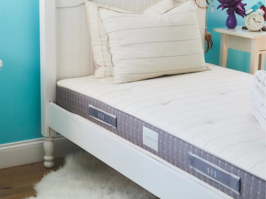 kid's bed with a grey and white mattress and white headboard against a blue wall