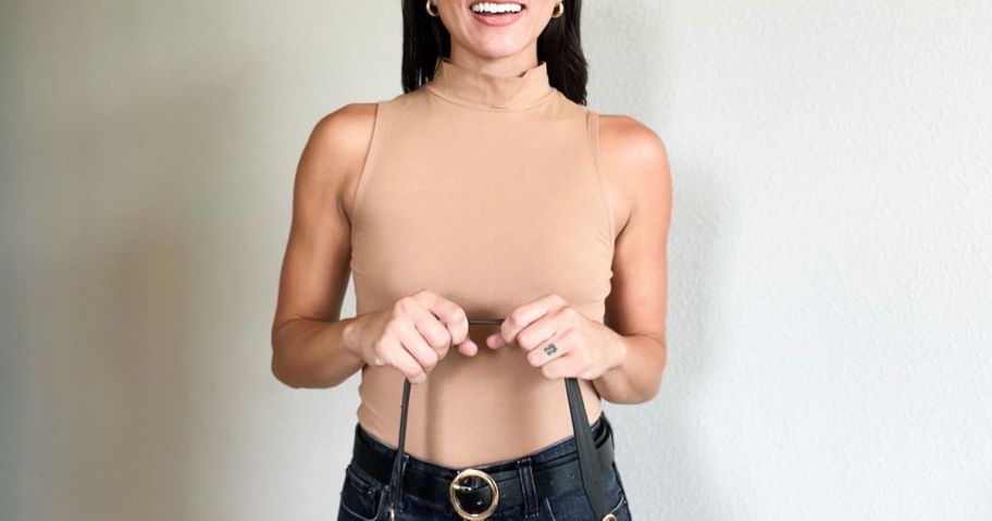 woman wearing a tan mock neck bodysuit with black jeans and holding a purse