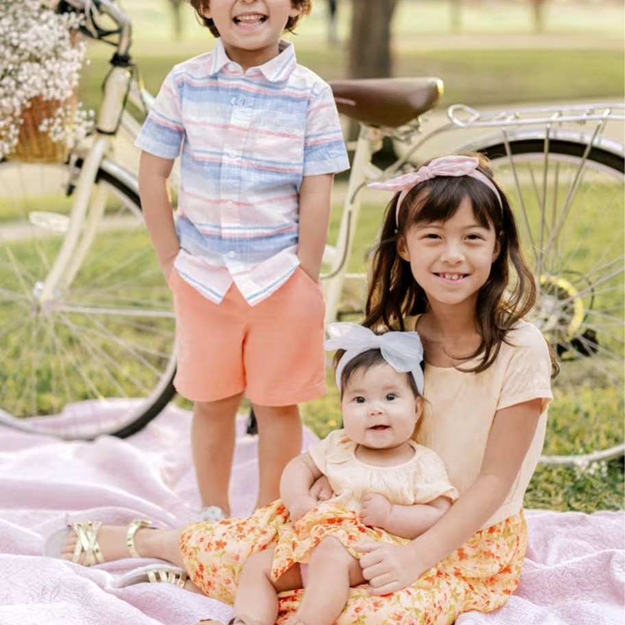 boy and two girls wearing matching easter clothes sitting on a pink blanket outdoors
