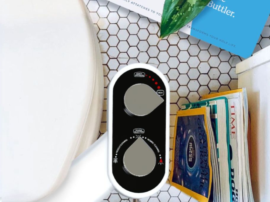 clear rear bidet attachment next to magazines in a bathroom