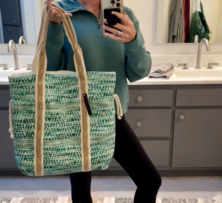 woman holding large beach tote in bathroom mirror
