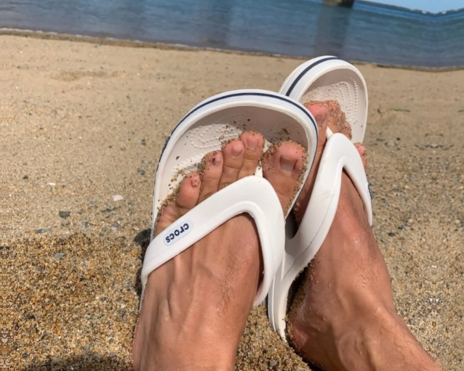 feet in sand wearing white crocs