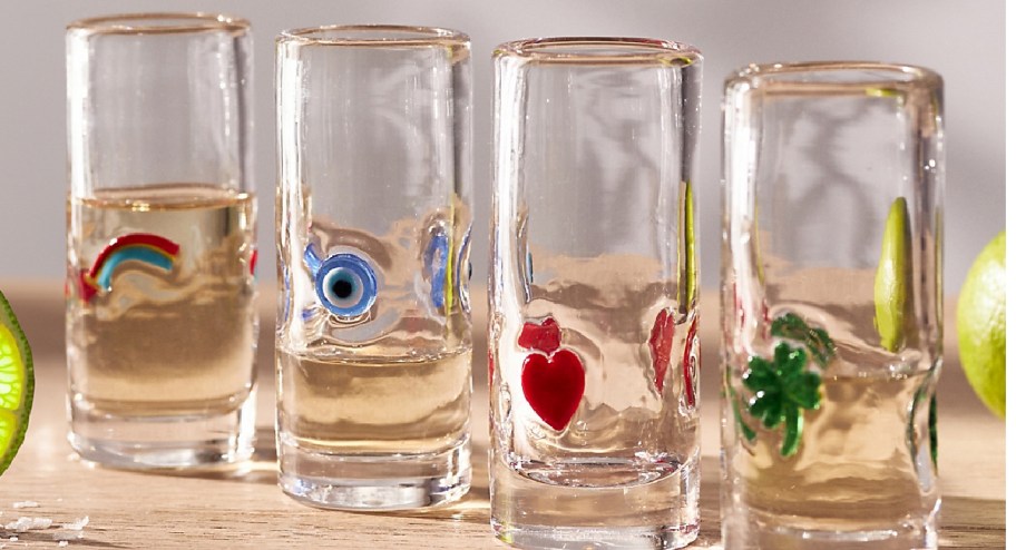 display of four shot glasses on a table with lime rids in the background