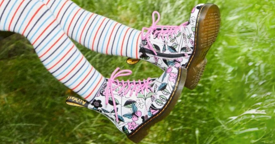 little girl's legs swinging over grass, wearing a pair of white Dr. Marten's boots with flowers and butterflies on them and pink laces