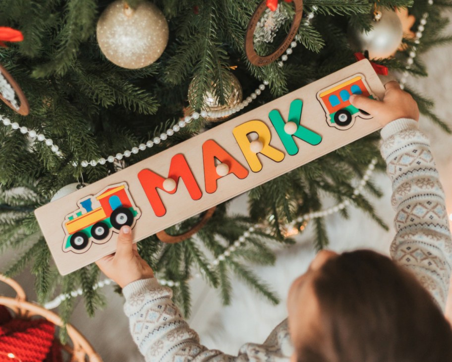 boy holding name puzzle near tree