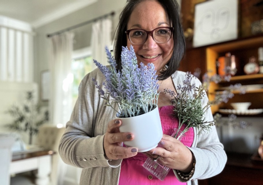 smiling woman standing in a home holding potted faux plants from target