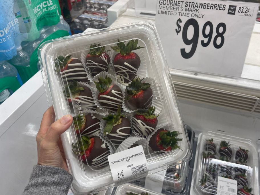 a womans hand holding a package of chocolate dipped strawberries