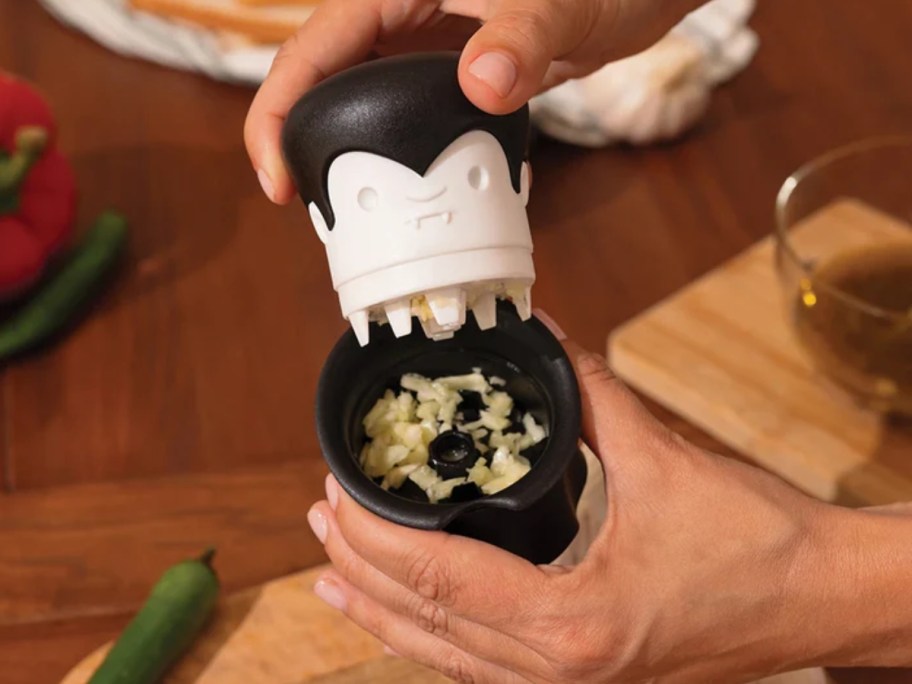 hands holding a vampire looking garlic crusher kitchen gadget with his head off, showing minced garlic inside