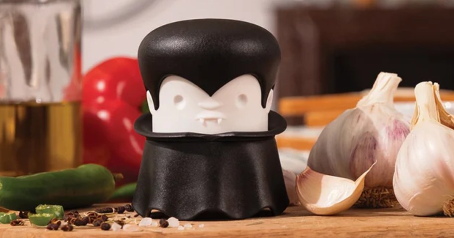 vampire garlic crusher kitchen gadget on counter with garlic and other foods behind him