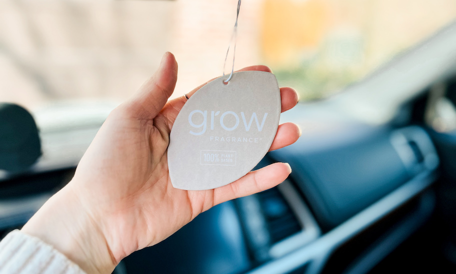 hand holding a grow fragrance air freshener hanging from mirror