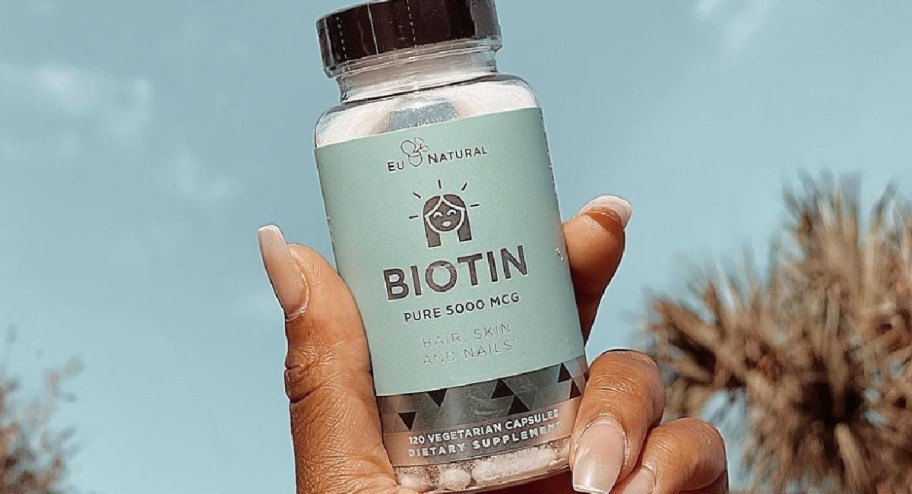 hand holding biotin pills while standing outside