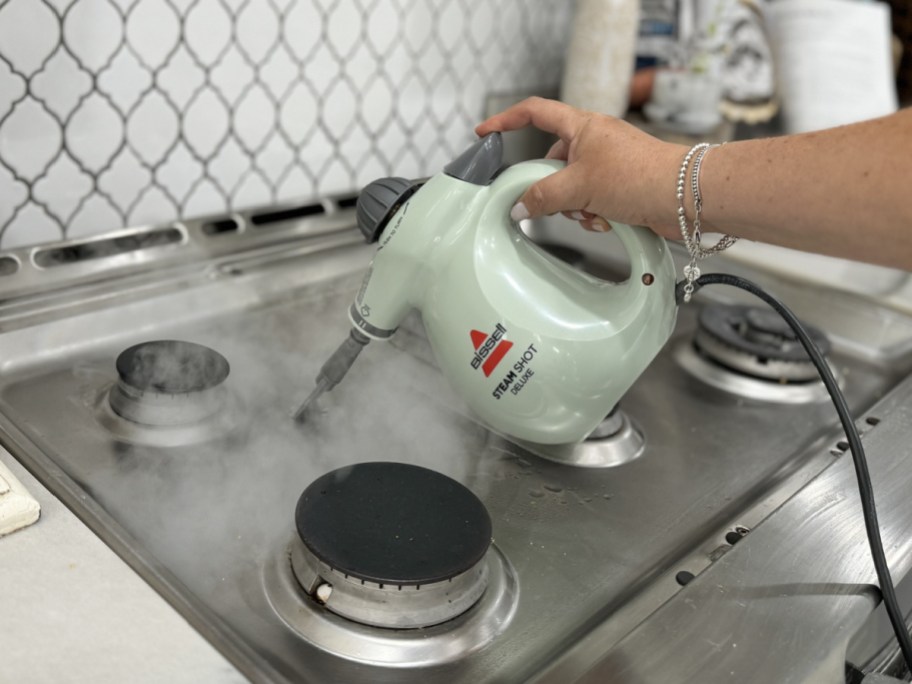hand holding bissell steamer on stove to clean it