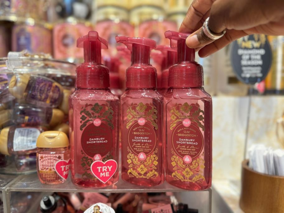 bath and body works foaming hand soaps on display in store with a hand touching the top of one of them