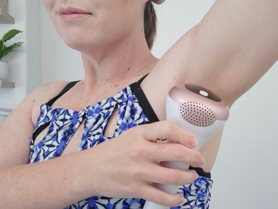 woman using pink and white hair removal tool under armpits