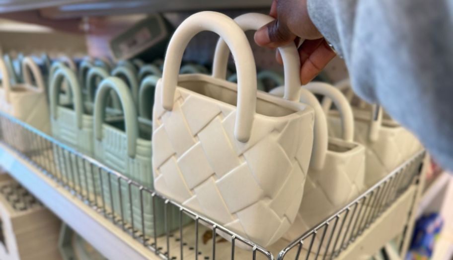 a womans hand reaching for a ceramic ivory colored hand bag vase